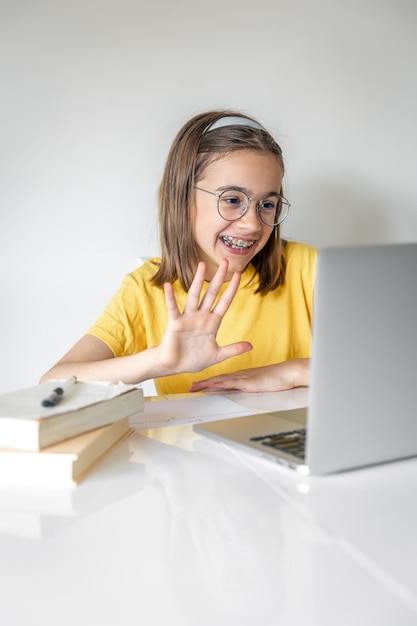 Une fille caucasienne souriante ayant un appel vidéo dans une salle de classe à distance à l'aide d'un ordinateur portable