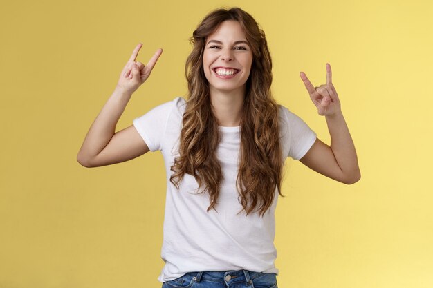 Fille chanceuse charismatique enthousiaste s'amusant profiter d'un spectacle de musique impressionnant geste rock-n-roll souriant ravi comme danse heavy-metal optimiste debout positif diverti fond jaune