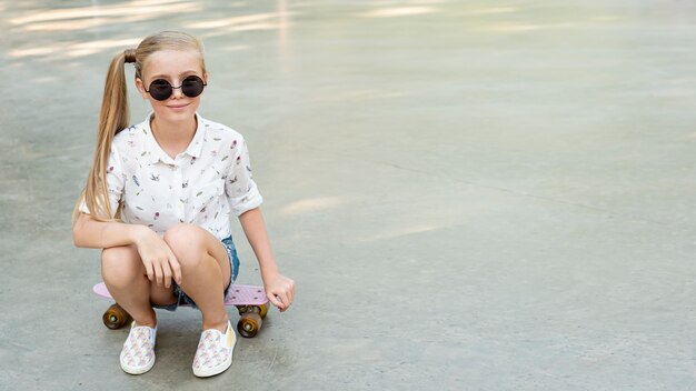 Fille avec une chemise blanche assise sur une planche à roulettes