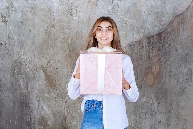 Fille en chemise blanche tenant une boîte-cadeau rose enveloppée d'un ruban blanc.