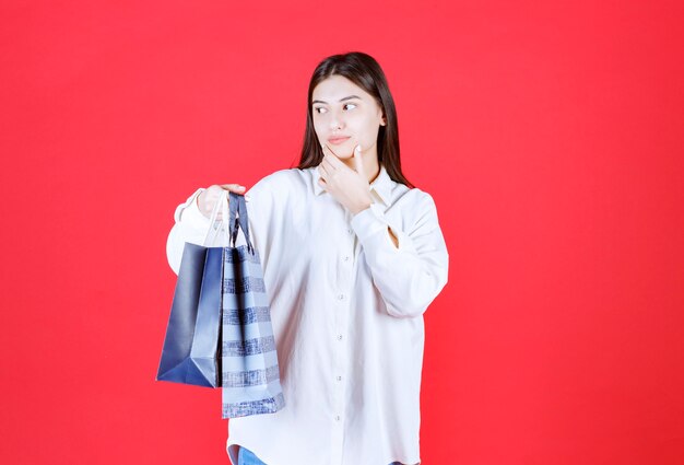 Fille en chemise blanche tenant plusieurs sacs à provisions et semble confuse et hésitante