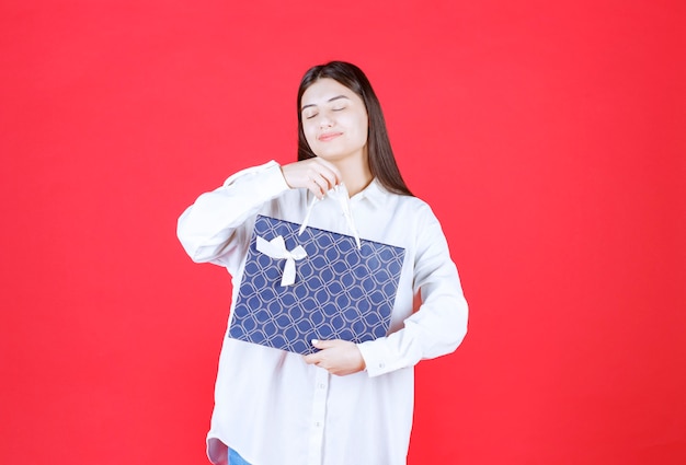 Fille en chemise blanche tenant un sac à provisions bleu et a l'air somnolent et fatigué