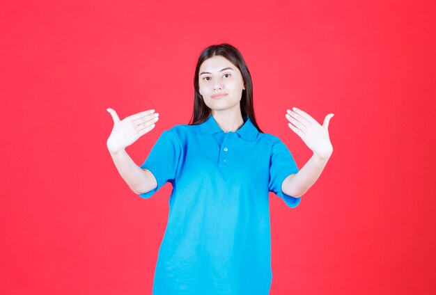 Fille en chemise bleue debout sur fond rouge et se pointant sur elle-même