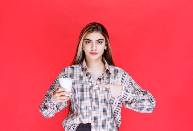 Fille en chemise à carreaux tenant une tasse de café jetable blanche