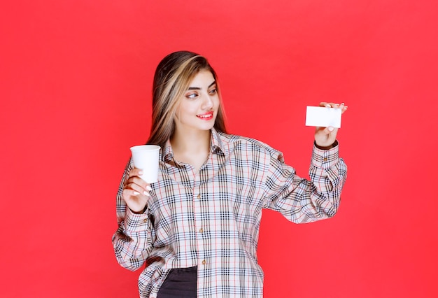 Fille en chemise à carreaux tenant une tasse de café et présentant sa carte de visite