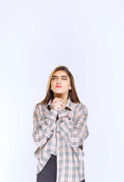 Fille en chemise à carreaux unissant les mains et priant