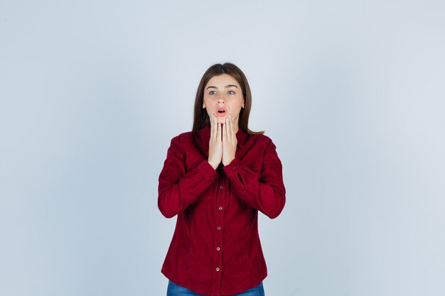 fille en chemise décontractée tenant les mains sur le menton, regardant loin et l'air surpris