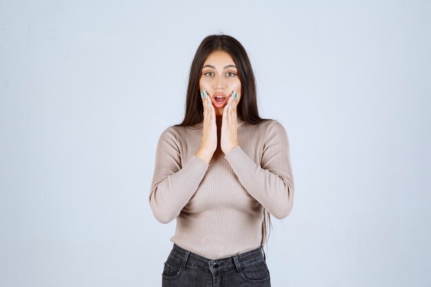 Fille en chemise grise a l'air excitée et surprise.