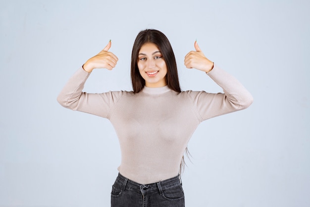 Fille en chemise grise faisant signe de pouce vers le haut.