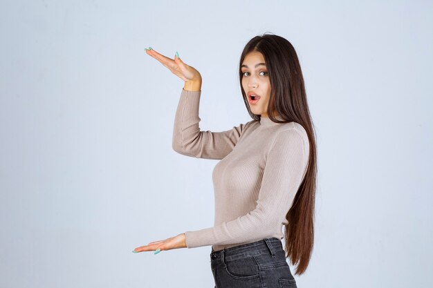 Fille en chemise grise montrant la hauteur d'un objet.