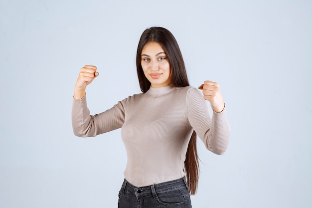 Fille en chemise grise montrant ses muscles du bras.