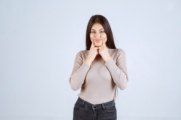 Fille en chemise grise pointant sur sa bouche.