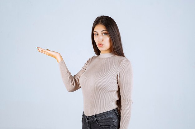 Fille en chemise grise pointant vers quelque chose sur la gauche.