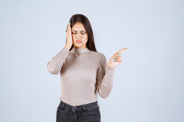 Fille en chemise grise tenant sa tête à cause de maux de tête.