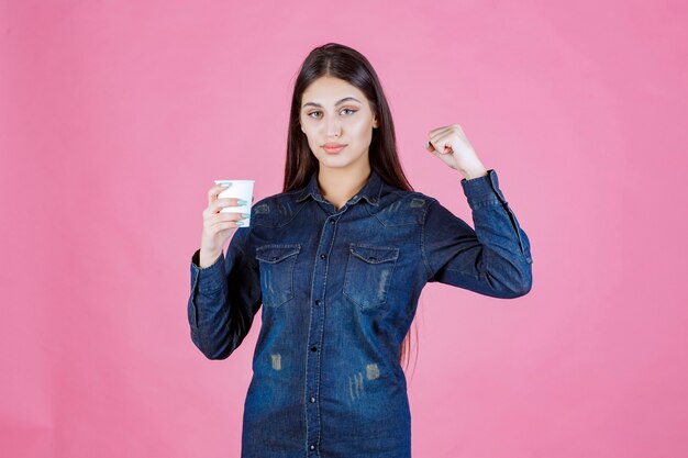 Fille en chemise en jean ayant une tasse de café et se sentant puissant