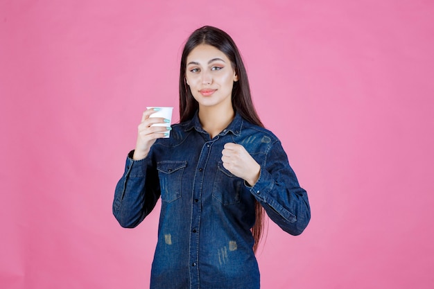 Fille en chemise en jean bénéficiant d'une tasse de café jetable