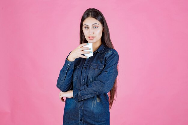 Fille en chemise en jean bénéficiant d'une tasse de café jetable