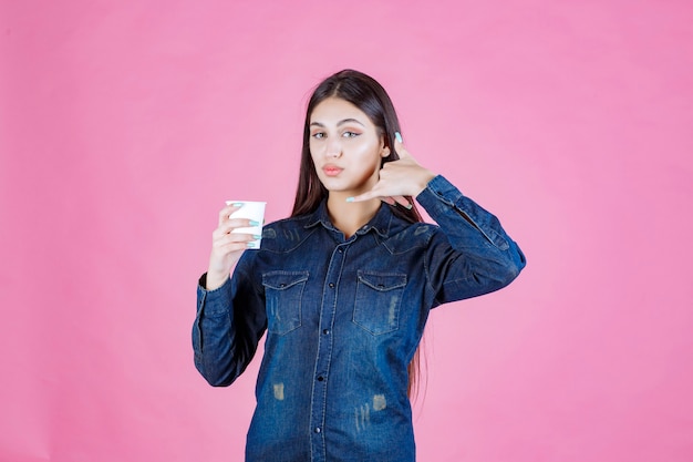 Fille en chemise en jean tenant une tasse de café et faisant l'indicatif d'appel