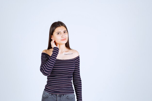 Fille en chemise rayée a l'air confuse et ravie.