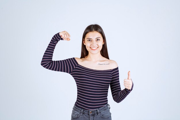 Fille en chemise rayée démontrant ses muscles du bras.