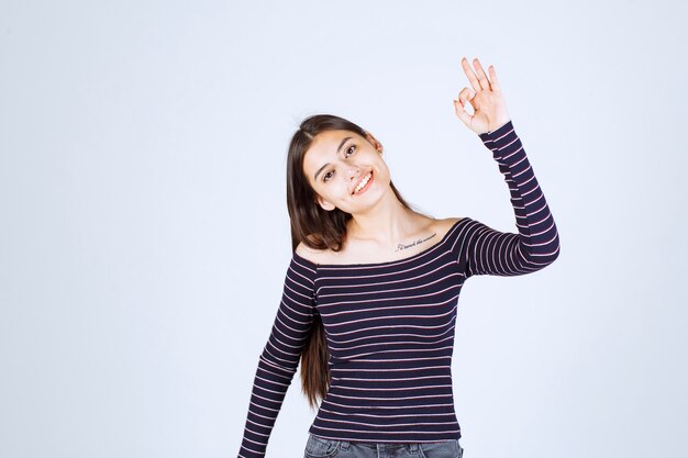 Fille en chemise rayée montrant un bon signe de jouissance.