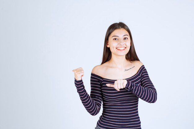 Fille en chemise rayée montrant quelque chose sur la gauche.