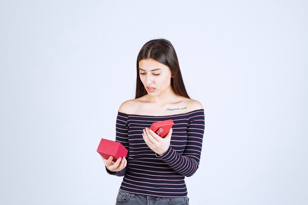 Fille en chemise rayée ouvre une boîte cadeau rouge et se confond.