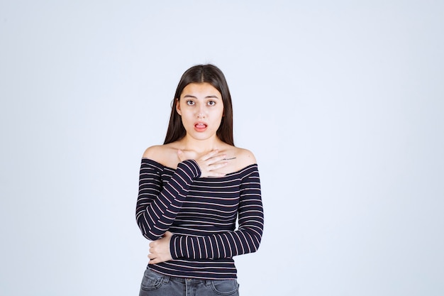 Fille en chemise rayée pointant sur elle-même.