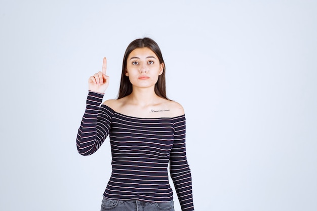 Fille en chemise rayée pointant vers le haut et montrant des émotions.