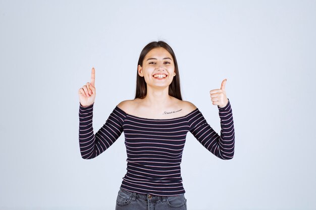 Fille en chemise rayée pointant vers le haut et montrant des émotions.