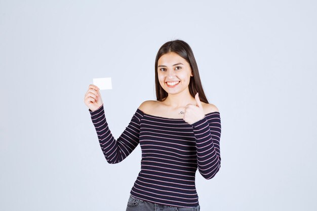 Fille en chemise rayée présentant sa carte de visite avec confiance.