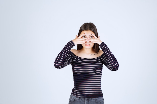 Fille en chemise rayée regardant à travers ses doigts.