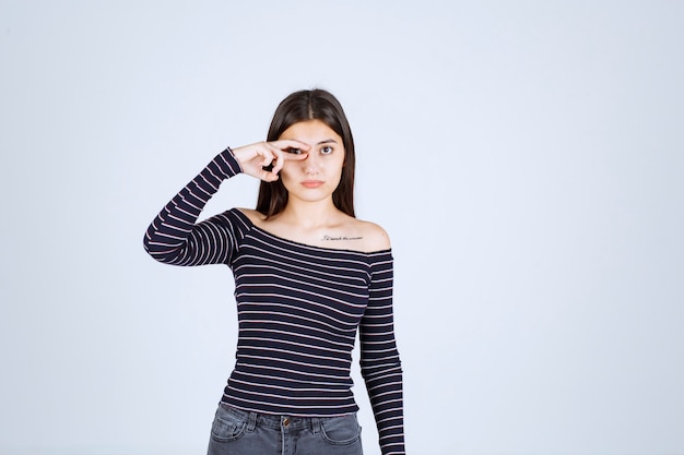 Fille en chemise rayée regardant à travers ses doigts.