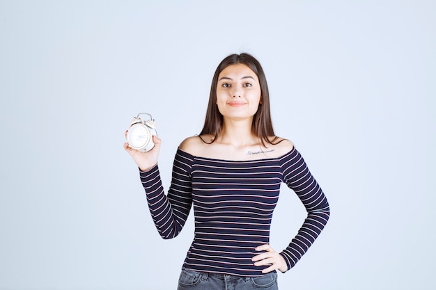 Fille en chemise rayée tenant un réveil et en faisant la promotion comme un nouveau produit.