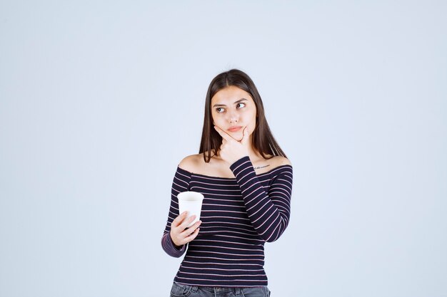 Fille en chemise rayée tenant une tasse de café en plastique et de la pensée.