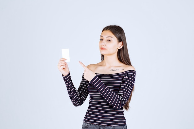 Fille en chemise rayée tient une carte de visite et pointe vers elle.