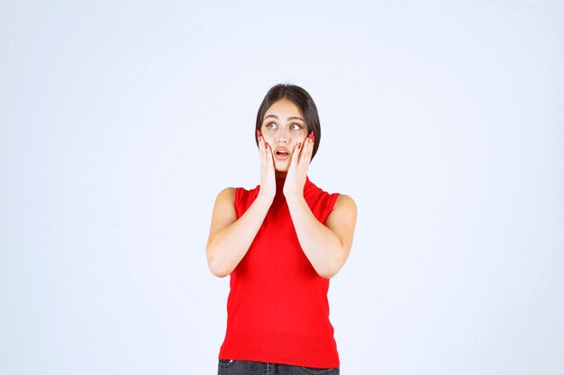 Une fille en chemise rouge a l'air effrayée et terrifiée.