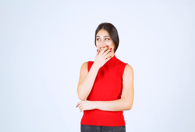 La fille en chemise rouge a l'air surprise par quelque chose d'inattendu.