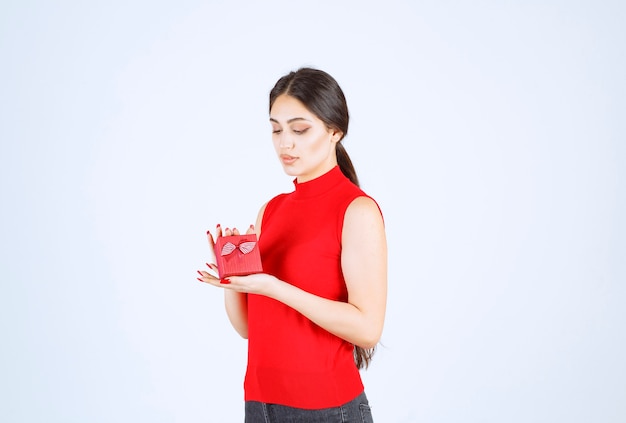 Fille en chemise rouge démontrant sa boîte cadeau rouge.