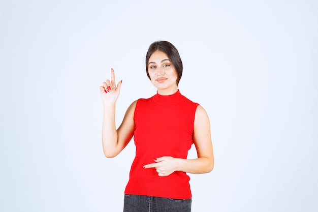 Fille en chemise rouge levant la main et pointant au-dessus.