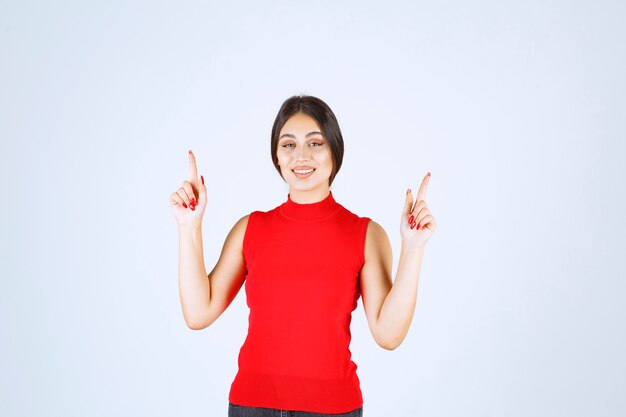 Fille en chemise rouge levant la main et pointant au-dessus.