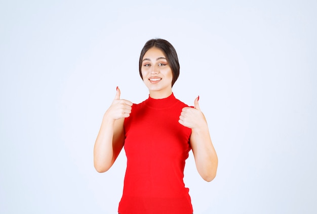 Fille en chemise rouge montrant les pouces vers le haut.