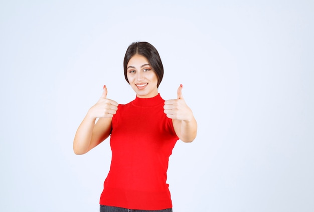 Fille en chemise rouge montrant les pouces vers le haut.