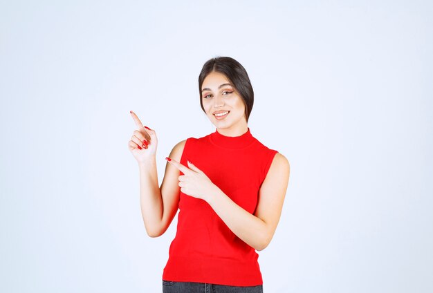 Fille en chemise rouge pointant vers quelque chose sur la gauche.