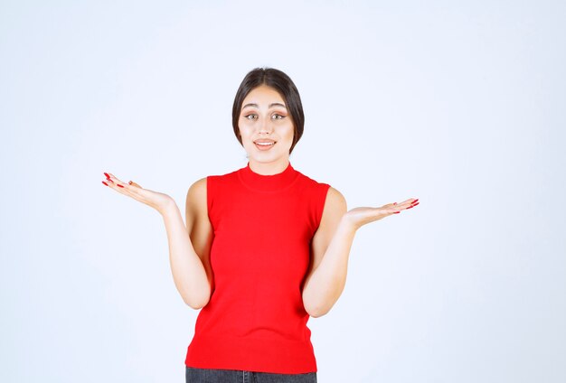 Fille en chemise rouge présentant et montrant quelque chose dans sa main.