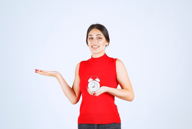 Fille en chemise rouge tenant et promouvant un réveil.