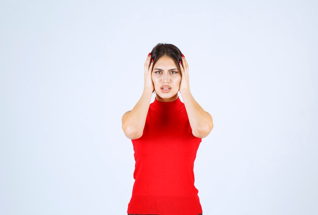 Fille en chemise rouge tenant sa tête avec les mains car elle a mal à la tête.