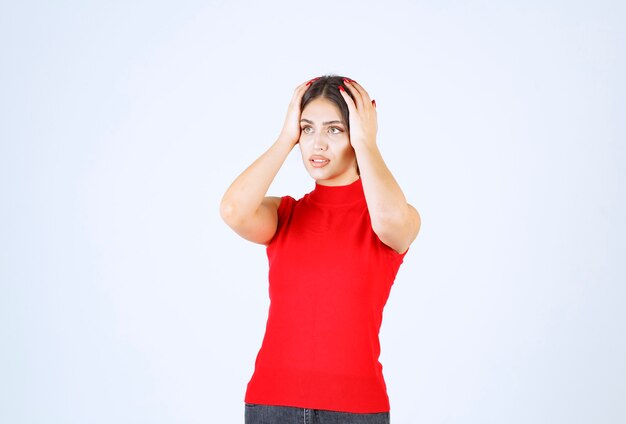 Fille en chemise rouge tenant sa tête avec les mains car elle a mal à la tête.