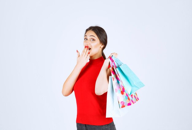 Fille en chemise rouge transportant des sacs colorés derrière son épaule.