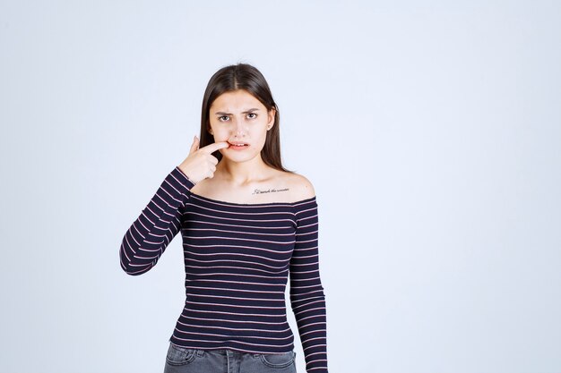 Fille en chemise srtiped a l'air malade et montre sa bouche.